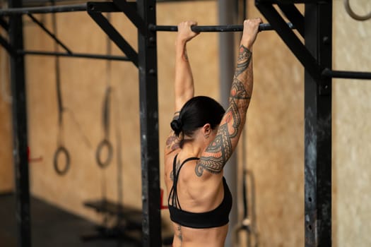 Rear side view of a sportive mature woman doing pull ups in the gym