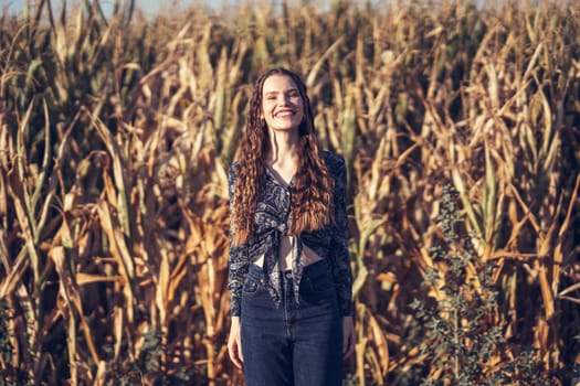 A joyful young woman beams brightly as she stands amidst a lush golden cornfield, perfectly capturing the essence of rural beauty along with the blissful, carefree moments that we truly cherish