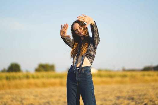 A cheerful young woman joyfully strikes a playful pose in a sunlit field, perfectly capturing the essence of summer, joy, spontaneity, and the feeling of unrestricted freedom that comes with it