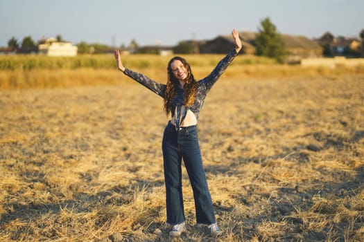 A cheerful young woman poses with her arms raised high in a stunning golden grass field, radiating pure joy and a deep sense of freedom while basking under the warm, inviting sunlight