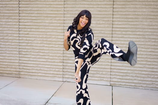 Hispanic adult female energetic dancer kicking in the air while performing happily in the city street