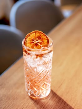 Transparent pink alcohol cocktail with ice, vodka and gin-tonic on bar counter in restaurant interior. Alcohol cocktail decorated orange slice. Cold alcoholic cocktail in bar or nightclub. Copy space