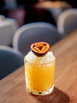 Yellow old-fashioned refreshing cocktail with whiskey and crushed ice on bar counter. Vertical. Alcohol or non-alcohol cold cocktail decorated passion fruit. Copy space.