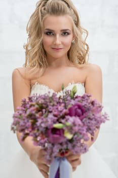 Gorgeous young bride posing in studio with an exquisite pink and violet bouquet