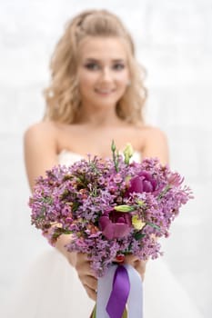 Gorgeous young bride posing in studio with an exquisite pink and violet bouquet tied with ribbons