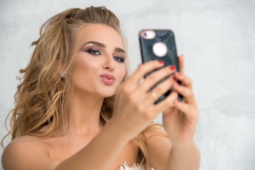 Beautiful bride holding sell phone in her hands and making selfie in studio