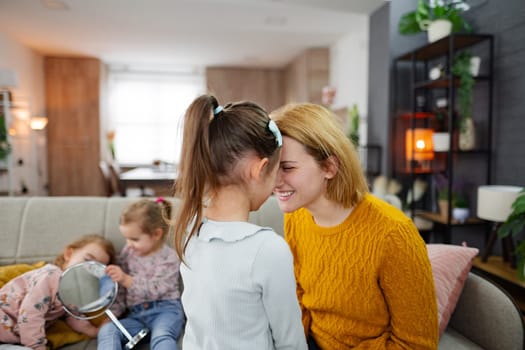 Mother in close contact with her eldest daughter, while the other two twin daughters sit on the couch in the background of the living room.