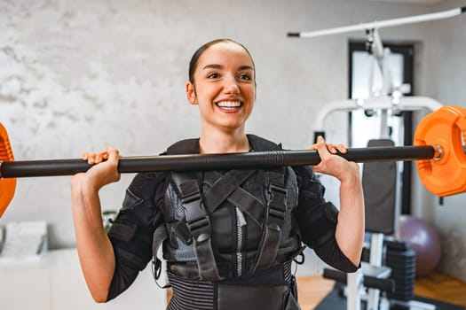 A woman joyfully lifts weights while wearing EMS training gear.