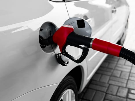 Red fuel nozzle pumping gasoline into white car at gas station.