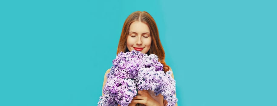 Portrait of beautiful woman enjoying smell of fresh bouquet lilac flowers on blue background