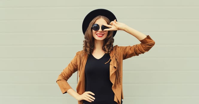 Fashion portrait of beautiful happy young woman, stylish girl smiling in black round hat posing on gray background