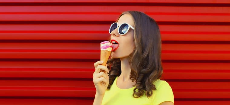 Summer portrait of happy young woman enjoying eating ice cream in glasses on red background