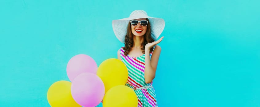 Beautiful happy laughing young woman with bunch of balloons in colorful dress on blue background