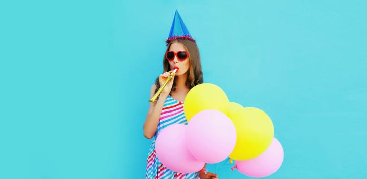 Portrait of cheerful young woman in a birthday cap with colorful balloons on a blue background