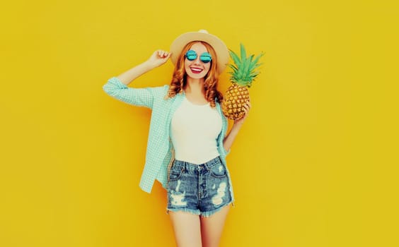 Happy smiling woman with pineapple having fun in summer hat, shorts on colorful yellow background