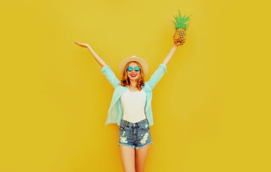 Happy cheerful woman raises her hands up with pineapple have fun in summer hat on yellow background