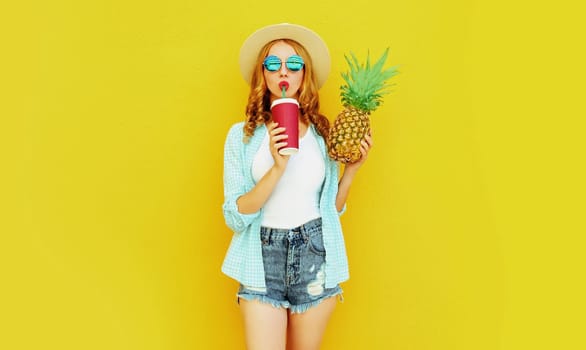 Portrait young woman drinking juice, holding pineapple in summer hat on colorful yellow background