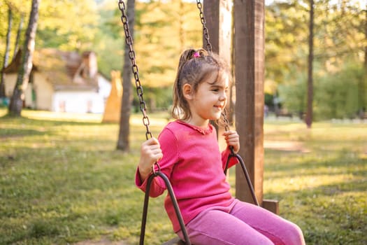 Cute smiling girl on a swing in the playground.