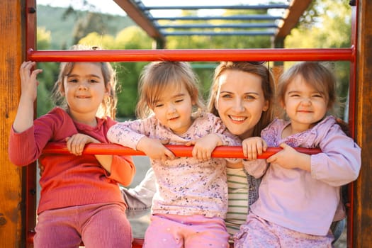 Smiling and happy mom with her older preschool daughter and twins on the playground.