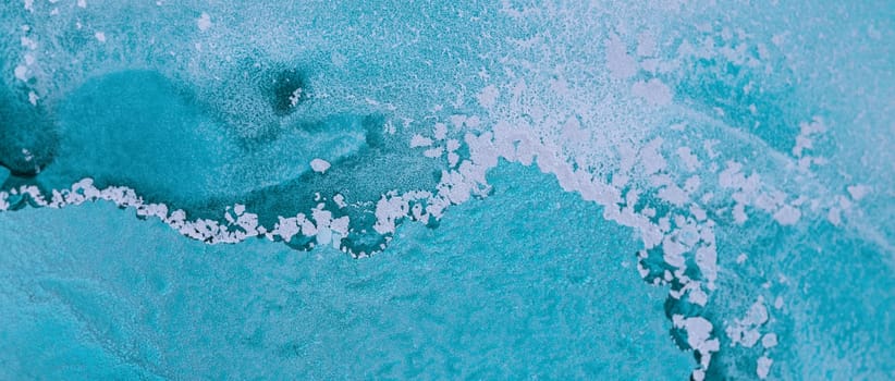 The intricate patterns of icy blue water at the edge of a frozen body, highlighting the delicate frost formations against a vibrant backdrop.