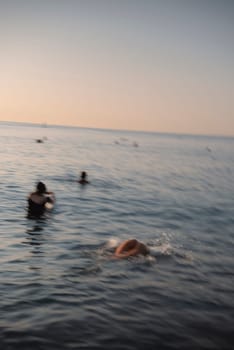 A serene, peaceful scene encompassing swimmers joyfully enjoying the tranquil waters of the sea at sunset