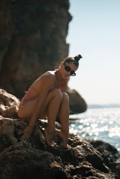 A woman wearing a stylish bikini is relaxing peacefully by the shimmering, beautiful blue sea on a warm, sunny day
