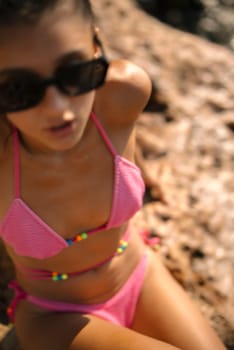 A fashionable young girl wearing a bright pink bikini joyfully enjoys the warm summer sun while relaxing by the rocks