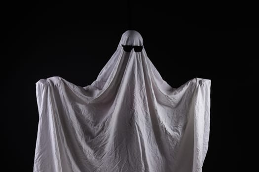 Person in costume of ghost pointing at something on dark background with space for text. Halloween celebration