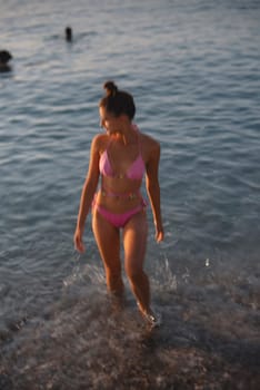 A woman enjoys her time at the beach, playfully walking in shallow water, wearing a stylish pink bikini