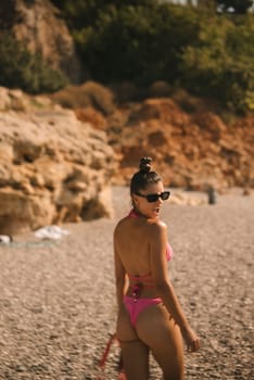 A confident woman strikes a pose in a vibrant pink bikini along the beautiful beach, surrounded by natural beauty