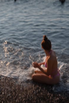 A young girl happily splashes around in the cool water, thoroughly enjoying a bright and sunny day by the sea