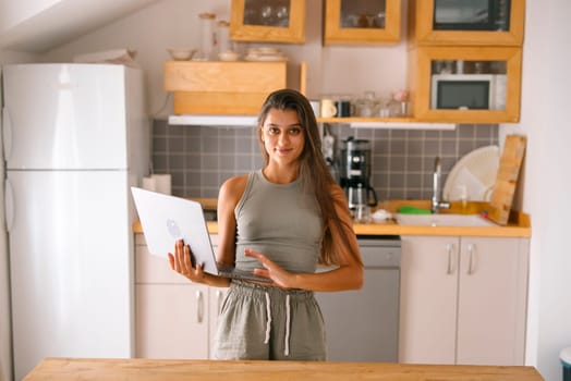 A fashionable young woman is actively engaging with her laptop in a stylish and contemporary kitchen setting