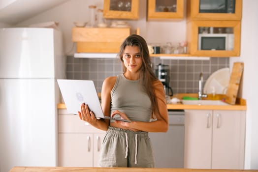 A stylish, modern young woman is actively engaging with her laptop while seated in a contemporary kitchen setting