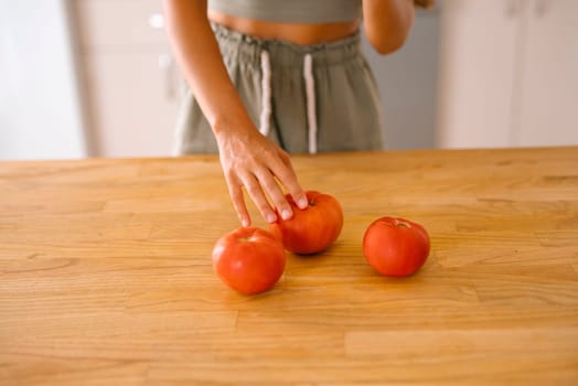 A hand carefully selecting ripe, fresh tomatoes on a rustic wooden kitchen table in a warm, inviting home