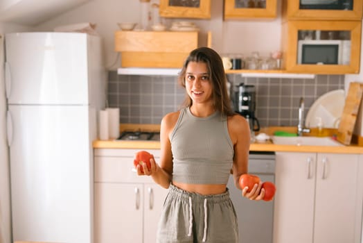 A woman joyfully holds vibrant, fresh tomatoes in her bright, modern kitchen, promoting concepts of healthy cooking