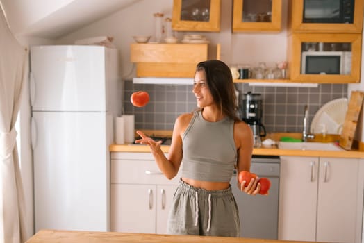 A joyful and cheerful woman is skillfully juggling bright red apples in a vibrant, modern kitchen space