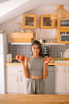 A vibrant young woman playfully holds fresh apples in her modern kitchen, embracing healthy eating choices
