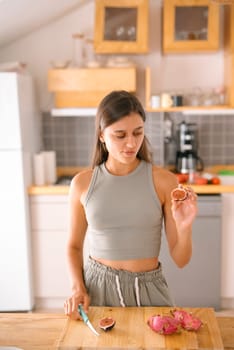 A young woman joyfully interacts with vibrant dragon fruit in a stylish, contemporary kitchen setting filled with light