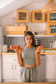 In a stylish kitchen, a young woman works out with dumbbells, showcasing a vibrant, healthy lifestyle