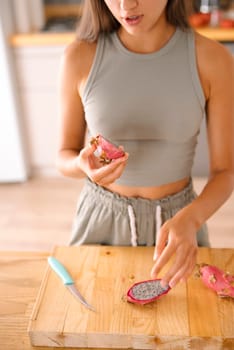 A woman is carefully preparing vibrant and exotic dragon fruit in a cozy and comfortable kitchen setting