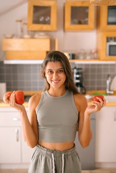 A cheerful woman holds a basket of apples in her modern kitchen, promoting healthy eating and wellness