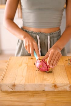 A skilled woman expertly slices through a vibrant and exotic dragon fruit while using a wooden cutting board