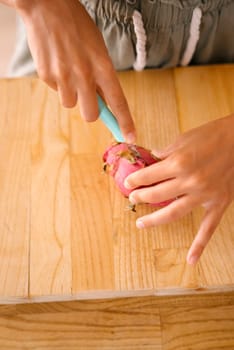 A person skillfully slicing a vibrant dragon fruit on polished wood, showcasing a delightful moment of freshness