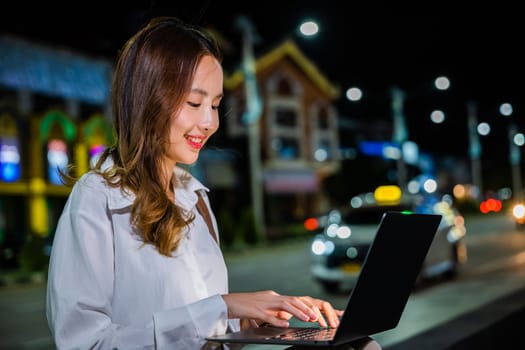 In the midst of a busy city street at night, a woman is working on her laptop computer, utilizing modern technology to maximize her productivity and connectivity.