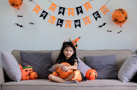 Cute little girl wearing a Halloween costume sits on the sofa with a happy. looking at the camera..