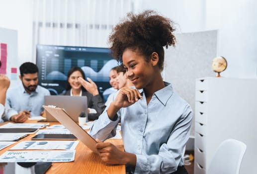 Portrait of happy young african businesswoman with group of office worker on meeting with screen display business dashboard in background. Confident office lady at team meeting. Concord