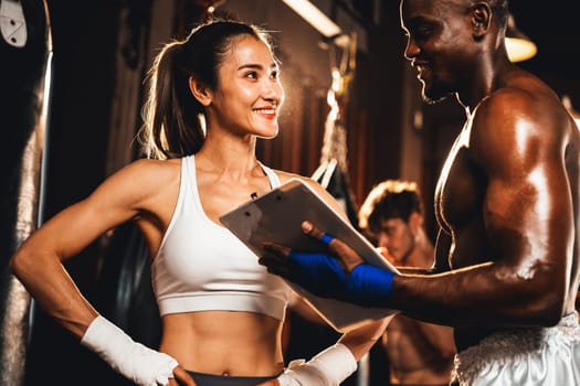 Asian female Muay Thai boxer and her personal boxing trainer discussing on her physical progress in the gym reflecting commitment to her body muscle growth and boxing performance. Impetus