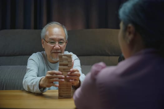 Happy grandparents Asian family enjoy playing toy block with little daughter together in home living room at night time, Smiling parent having fun play build constructor tower of wooden blocks