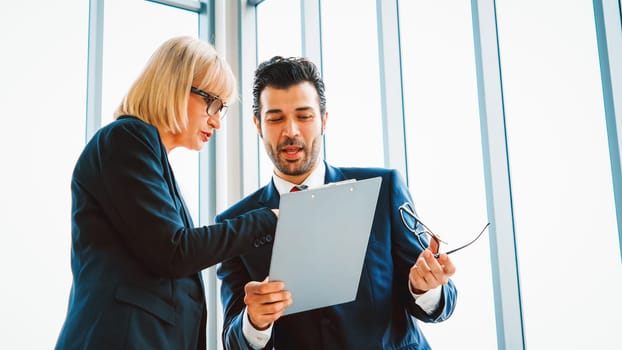 Two business people talk project strategy at office meeting room. Businessman discuss project planning with colleague at modern workplace while having conversation and advice on financial report. Jivy