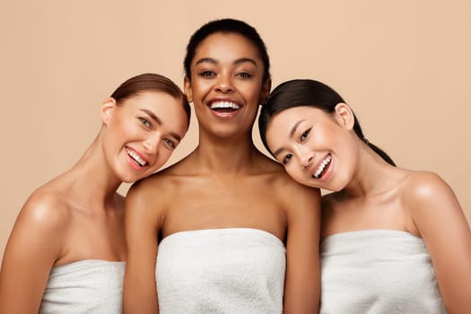 Beauty And Spa. Three Positive Pretty Girls Wrapped In Bath Towels Posing After Shower On Gray Background In Studio